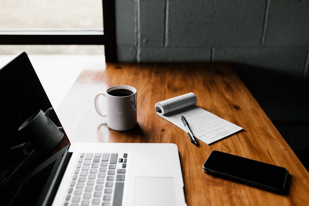 desk with a laptop, cup of coffee and notepad with a pen to write down blog ideas for a financial company.