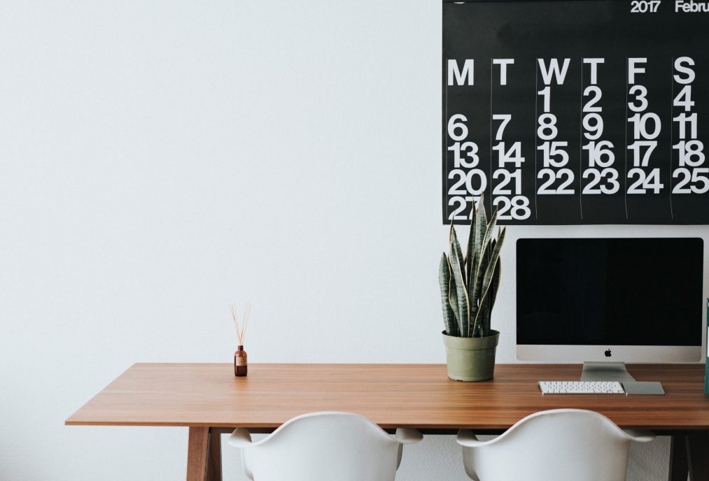 computer desktop on a table with a calendar on the wall